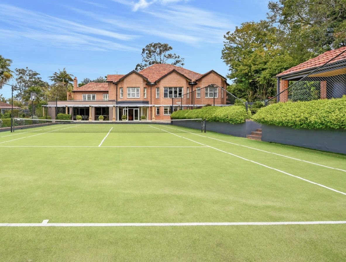 Brick residence behind a full-size grass tennis court